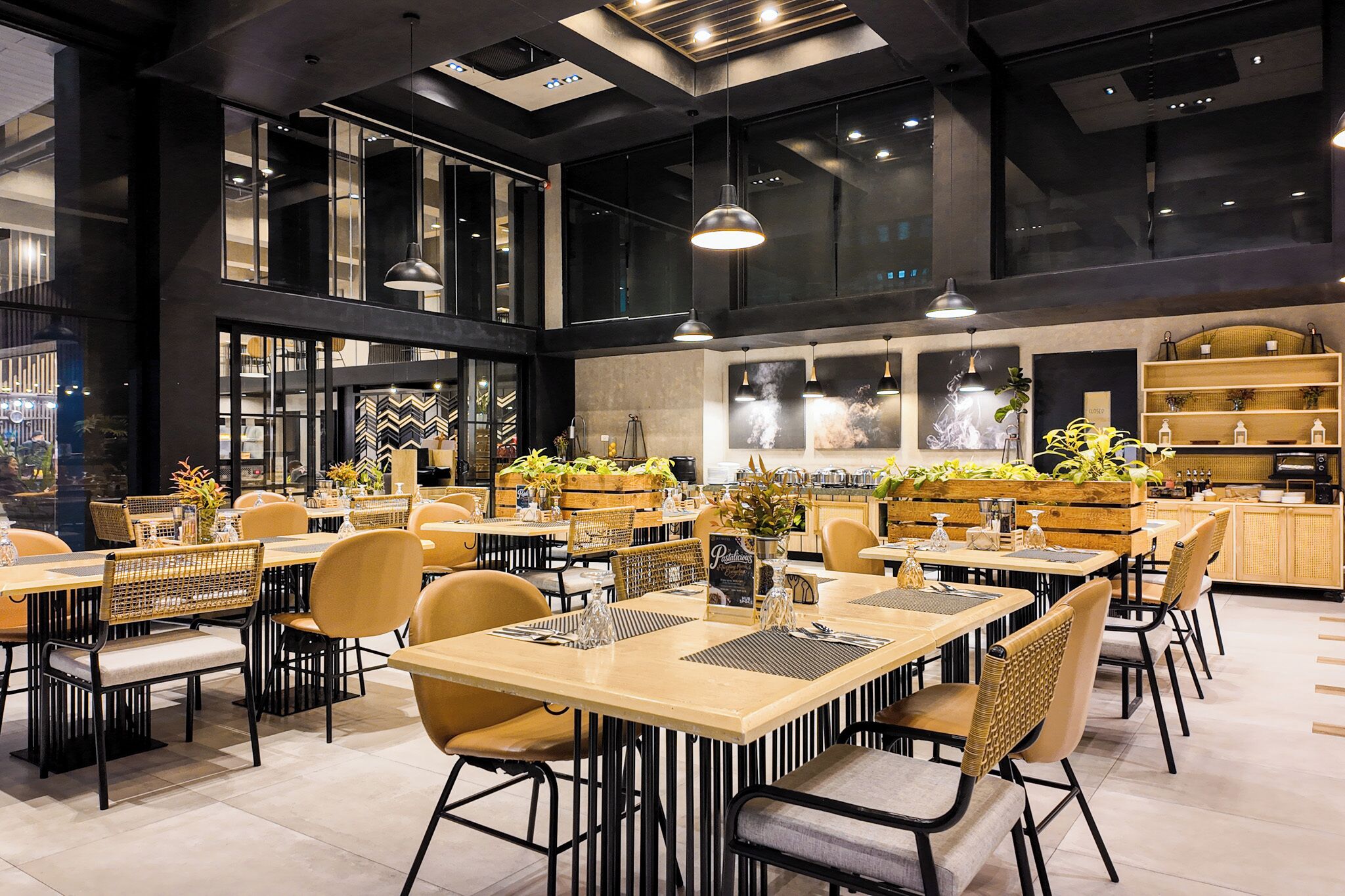 A modern restaurant with high ceilings, pendant lighting, and a central dining area with tables and chairs.