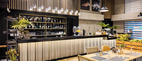 A modern bar area with a long counter, multiple hanging pendant lights, and a variety of bottles and glasses.