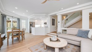 Ein modernes Wohnzimmer mit Sofa, Couchtisch, Esstisch und Stühlen. Im Hintergrund ist eine Küchenzeile mit Kühlschrank und Mikrowelle zu sehen.