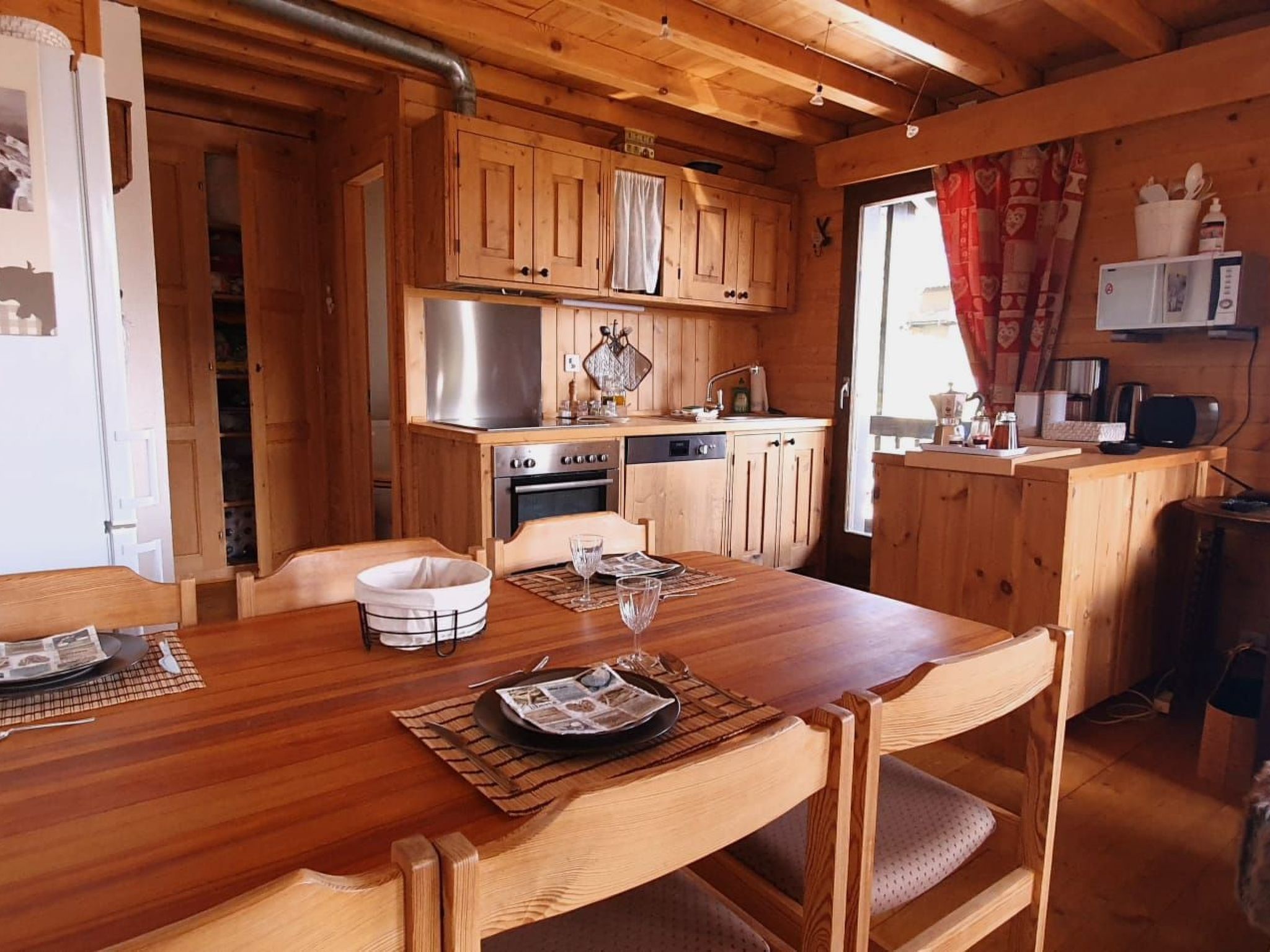 Ein Holzinterieur mit einem für zwei Personen gedecktem Esstisch, einer Küche mit Herd und Spüle sowie einer Mikrowelle auf der Arbeitsfläche.