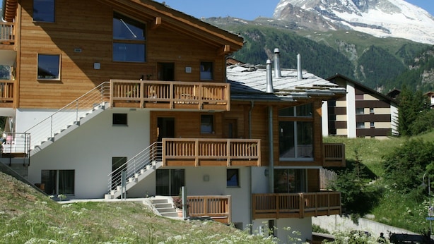 Un bâtiment en bois à plusieurs étages, doté de balcons, d’un escalier et offrant une vue sur une montagne enneigée.