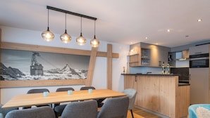 Une cuisine moderne avec des meubles en bois, un îlot central et un coin repas comprenant une table en bois et des chaises grises.