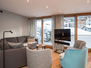 A modern living room with a sofa, armchair, and a flat-screen TV. - Haus Arctis, (Zermatt), 1855.02 by Interhome (Zermatt)