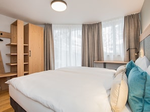 A bedroom with a large bed, wooden wardrobe, and a desk with a chair. - Haus Arctis, (Zermatt), 1855.02 by Interhome (Zermatt)