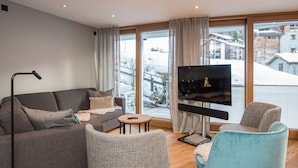 Un salon moderne avec un canapé, des fauteuils, un téléviseur et une vue sur un paysage enneigé.