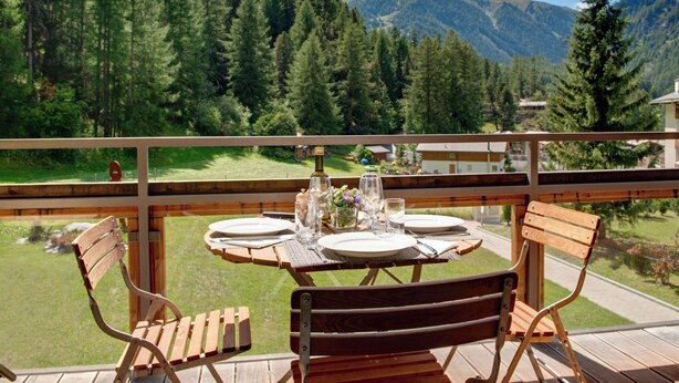 Una terraza de madera con una mesa lista para dos, con vista a un paisaje montañoso.