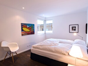 Une chambre à coucher moderne avec un lit, une chaise, un tableau et une fenêtre.