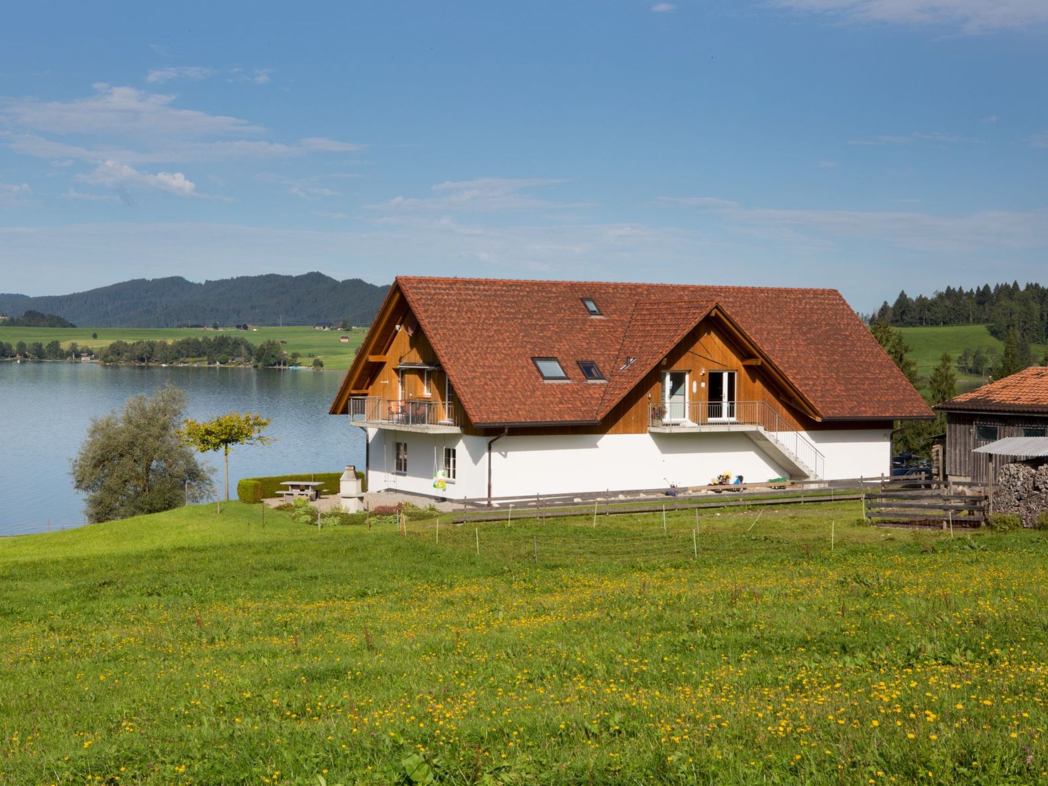 Una casa con techo inclinado, un balcón y vistas a un lago y montañas.