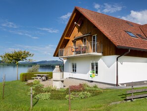A two-story wooden house with a balcony, a lake view, and a picnic table. - Ferienhof am See – Willerzell, (Willerzell), by Interhome (Willerzell)