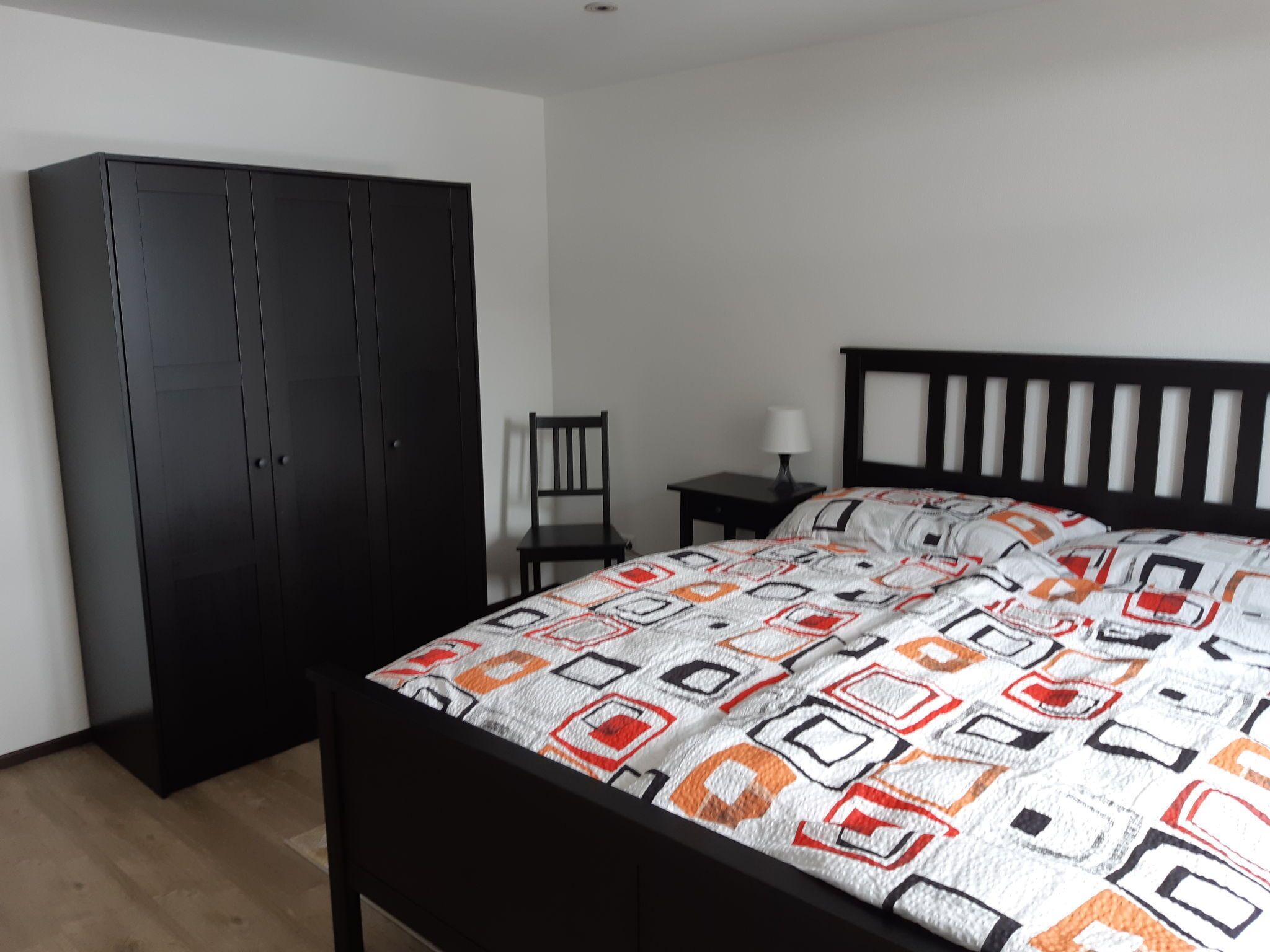 Ein Schlafzimmer mit einem Bett, einem Kleiderschrank, einem Sessel und einem Nachttisch.