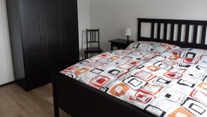 Un dormitorio con cama, armario, silla y mesita de noche.