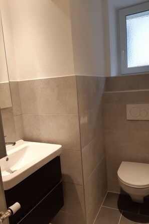 A bathroom with a white sink, dark cabinet, and a toilet. - Appartement - Le Pèlerin, (Saignelegier), by Interhome (Saignelegier)