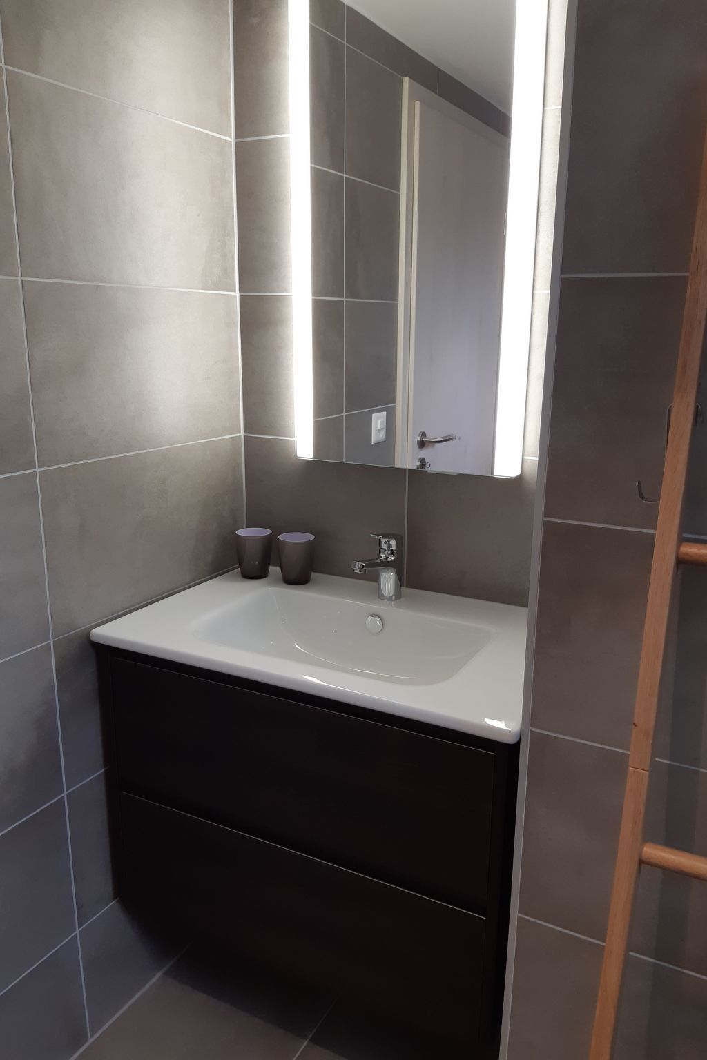 Une salle de bain avec un lavabo blanc, des meubles de rangement sombres et un miroir.