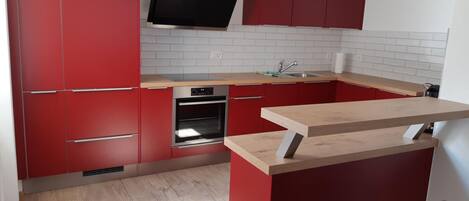 Uma cozinha moderna com armários vermelhos, forno embutido e bancada de madeira.