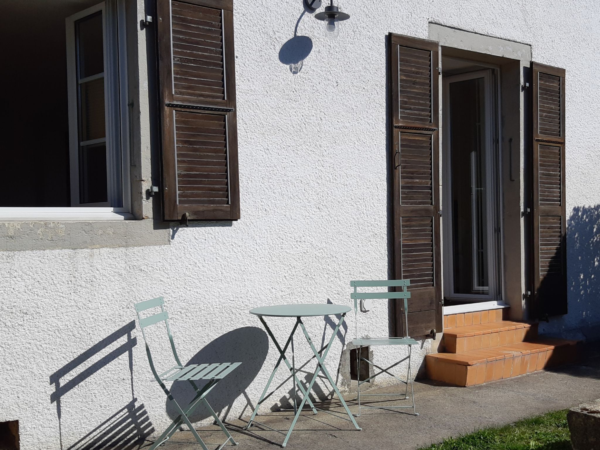 Ein Gebäude mit zwei offenen Fenstern, einem kleinen Tisch und Stuhl im Freien sowie einer Treppe, die zum Eingang f ührt.