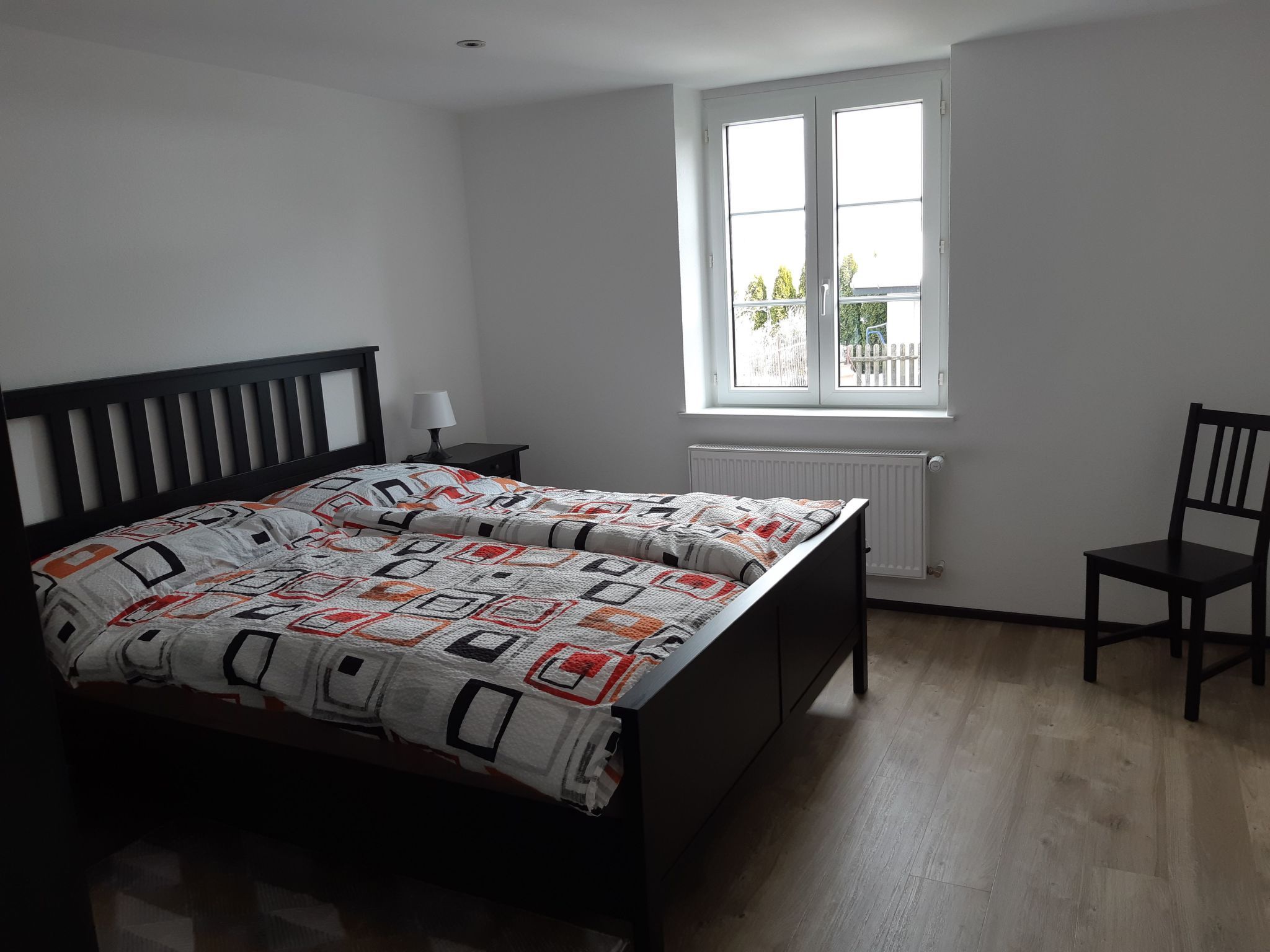 Una camera da letto con un letto, una finestra, un termosifone e una sedia.