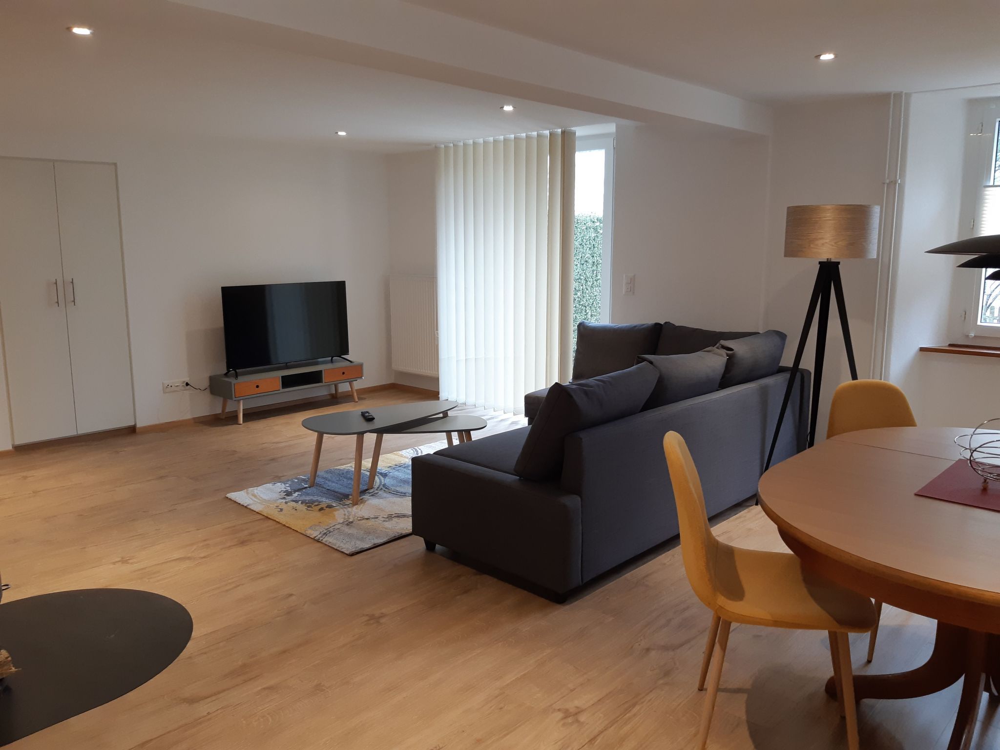 Ein modernes Wohnzimmer mit einer Couch, einem Fernseher, einem Esstisch und einer Lampe.