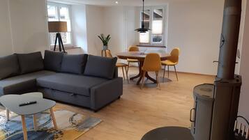 Ein Wohnzimmer mit einer Couch, einem Couchtisch, einem Esstisch mit Stühlen, einem Kamin und einem Fenster mit Jalousien.
