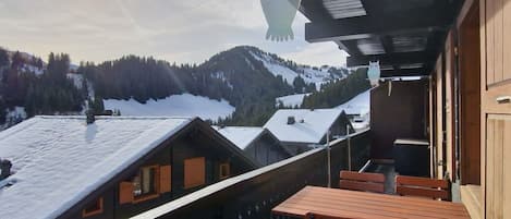 A wooden balcony with a view of snow-covered roofs and mountains.