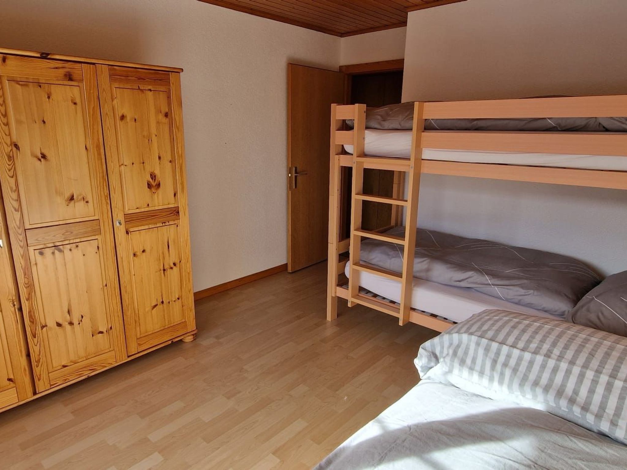 A room with a bunk bed, a wooden wardrobe, and a door.