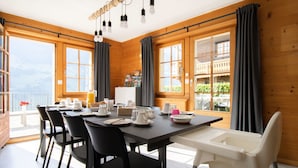 Un comedor con una mesa dispuesta para cuatro, paredes de madera, ventanas amplias con cortinas y vistas al exterior.