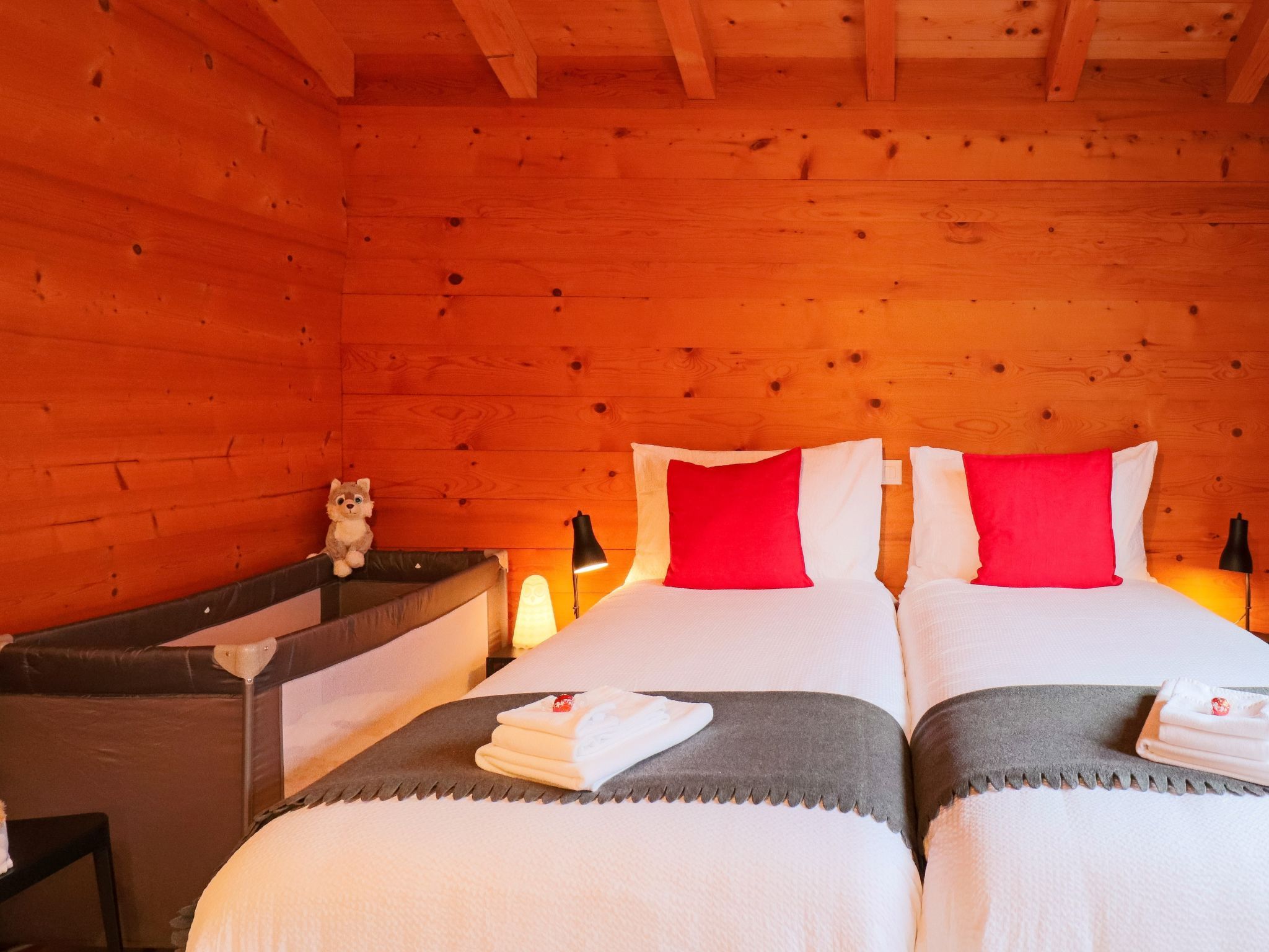 A wooden cabin room with two beds, a nightstand, and a lamp.