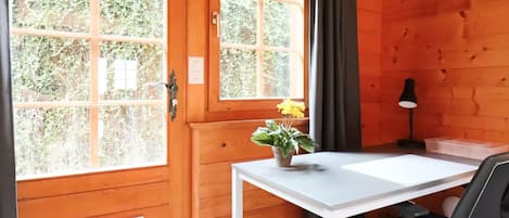 Une pièce en bois avec un bureau blanc, une chaise, une plante en pot et une fenêtre avec des rideaux.