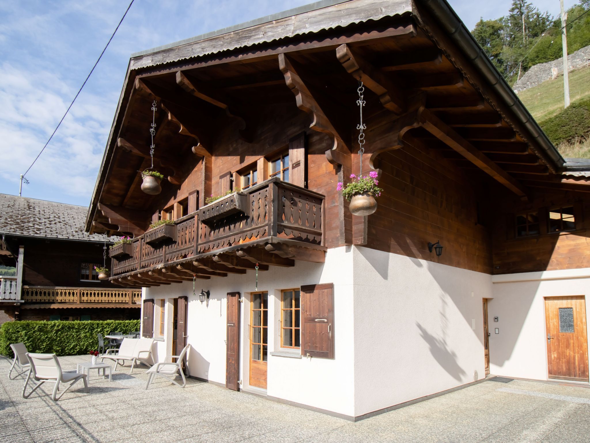 A traditional wooden chalet with a balcony, outdoor seating, and hanging flower pots.