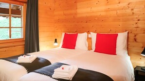 Una habitación de cabaña de madera con una cama, una ventana con cortinas y una mesita de noche con una lámpara.