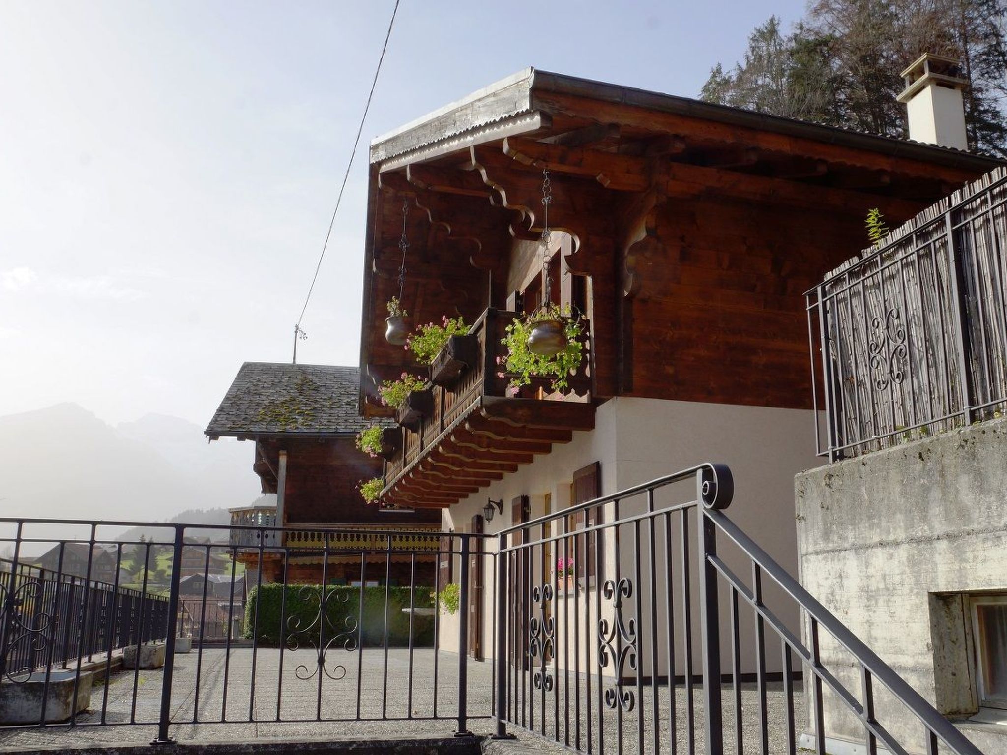 Un edificio de madera con balcón, una reja de metal y un paisaje montañoso de fondo.