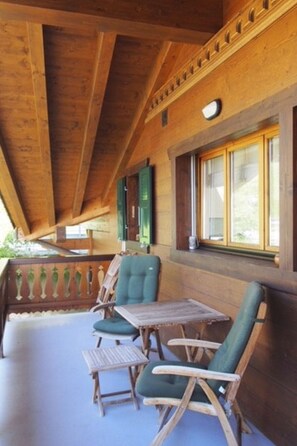 Ein Holzeinrichtung mit hoher Decke, ein Balkon mit grünen Fensterläden sowie eine Anordnung aus Tisch und Stühlen.