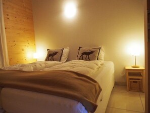 Quarto com cama, duas almofadas estampadas com padrões de animais, mesa de cabeceira e abajur.