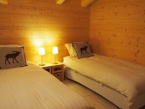 Ein Zimmer mit zwei Betten, jedes mit einem Kopfkissen mit Elchmuster, und zwei Nachttischlampen.