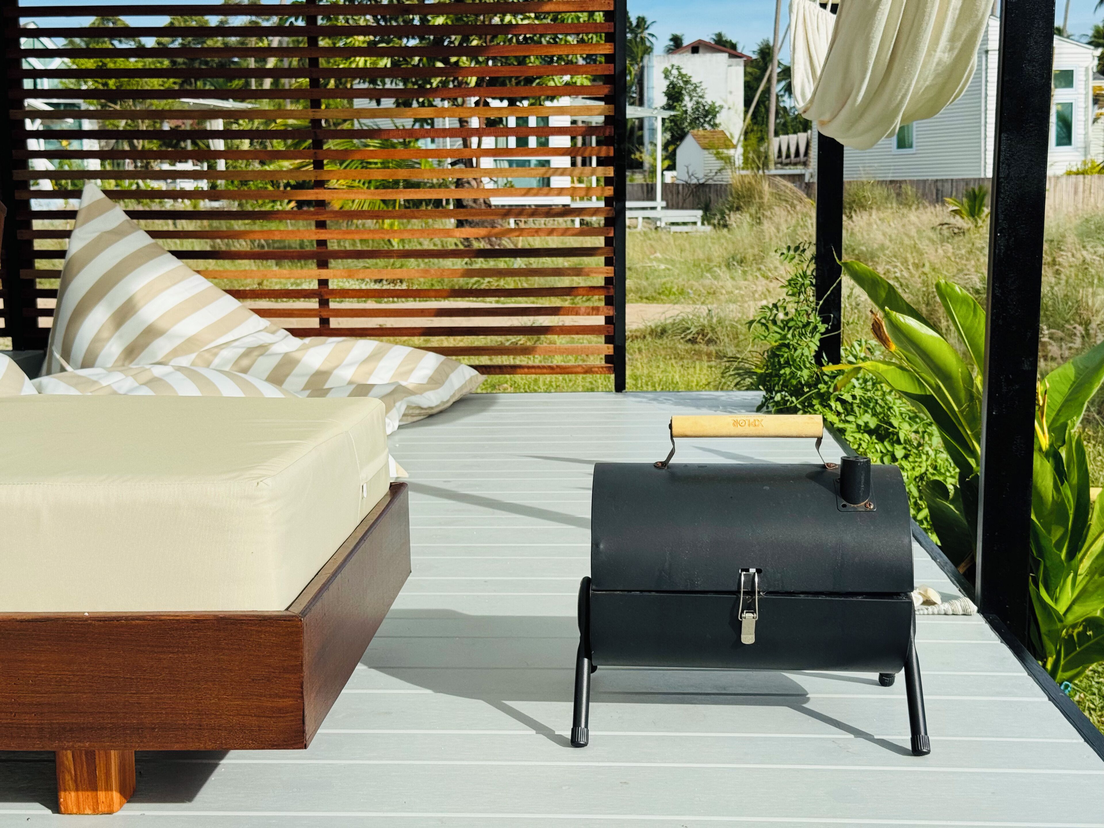 A deck with a bed and a grill, surrounded by a wooden fence and greenery.