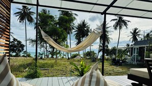 Una hamaca bajo techo, asientos exteriores con cojines y vistas a palmeras y al mar.