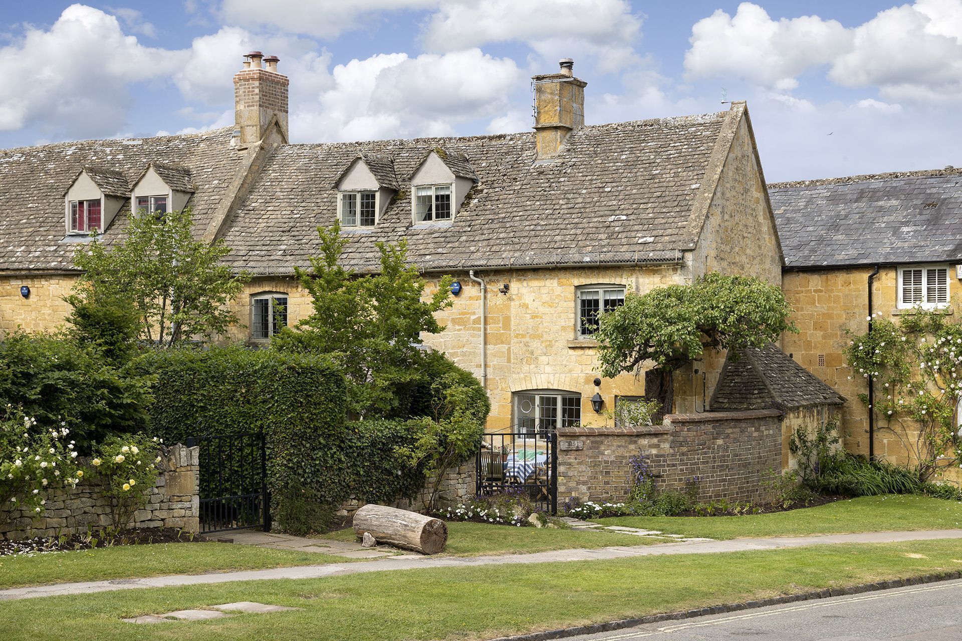 A traditional stone house with multiple chimneys, a front door, and a small garden with a bench and flowers.