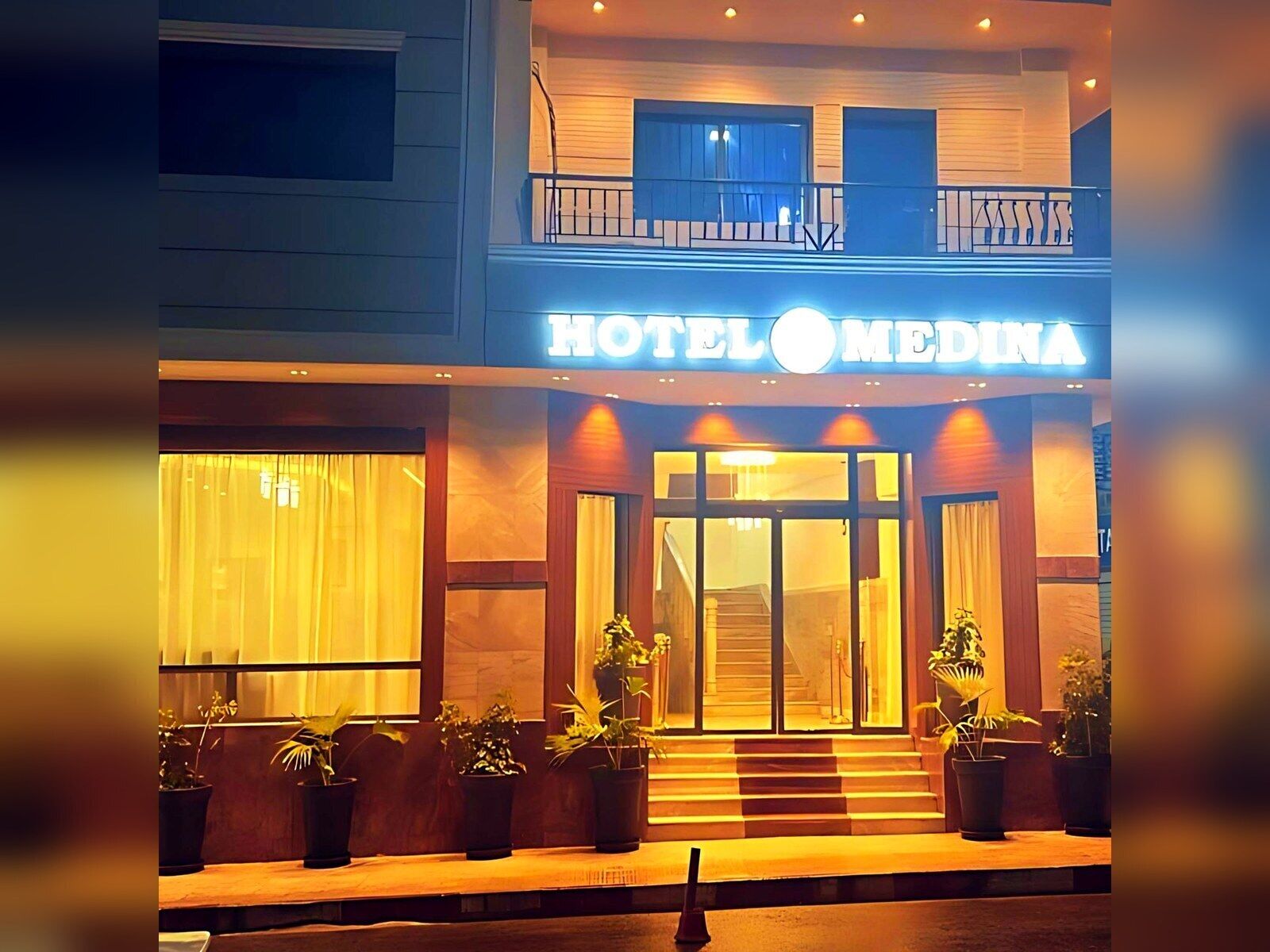 A hotel entrance with a sign reading 'HOTEL MEDINA,' a staircase leading to the entrance, and potted plants in front.