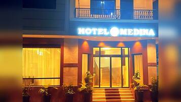 A hotel entrance with a sign reading 'HOTEL MEDINA,' a staircase leading to the entrance, and potted plants in front.