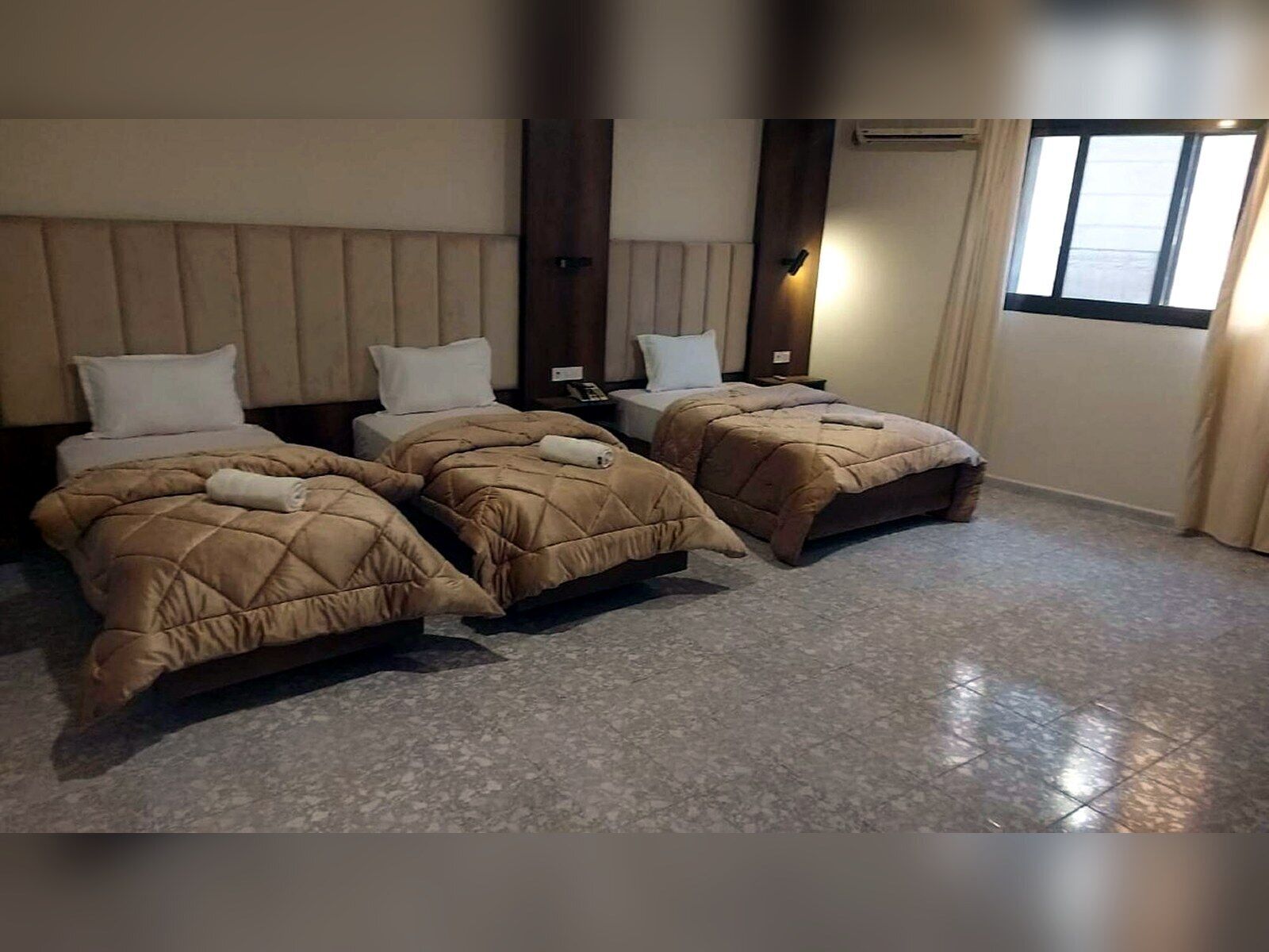 Ett hotellrum med tre sängar, ett stort fönster och en modern design.