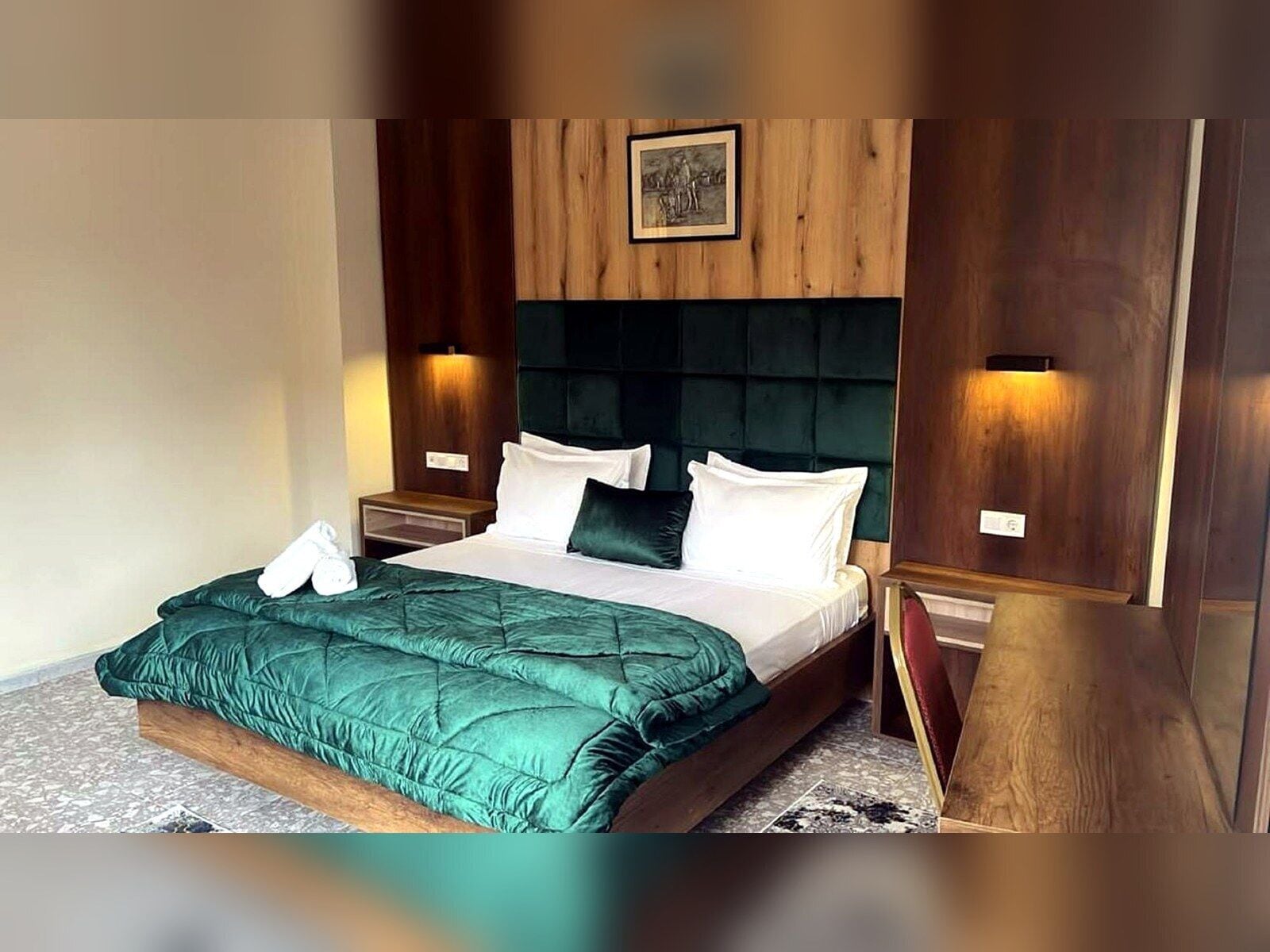 A hotel room with a bed, wooden headboard, two bedside tables, and a picture on the wall.