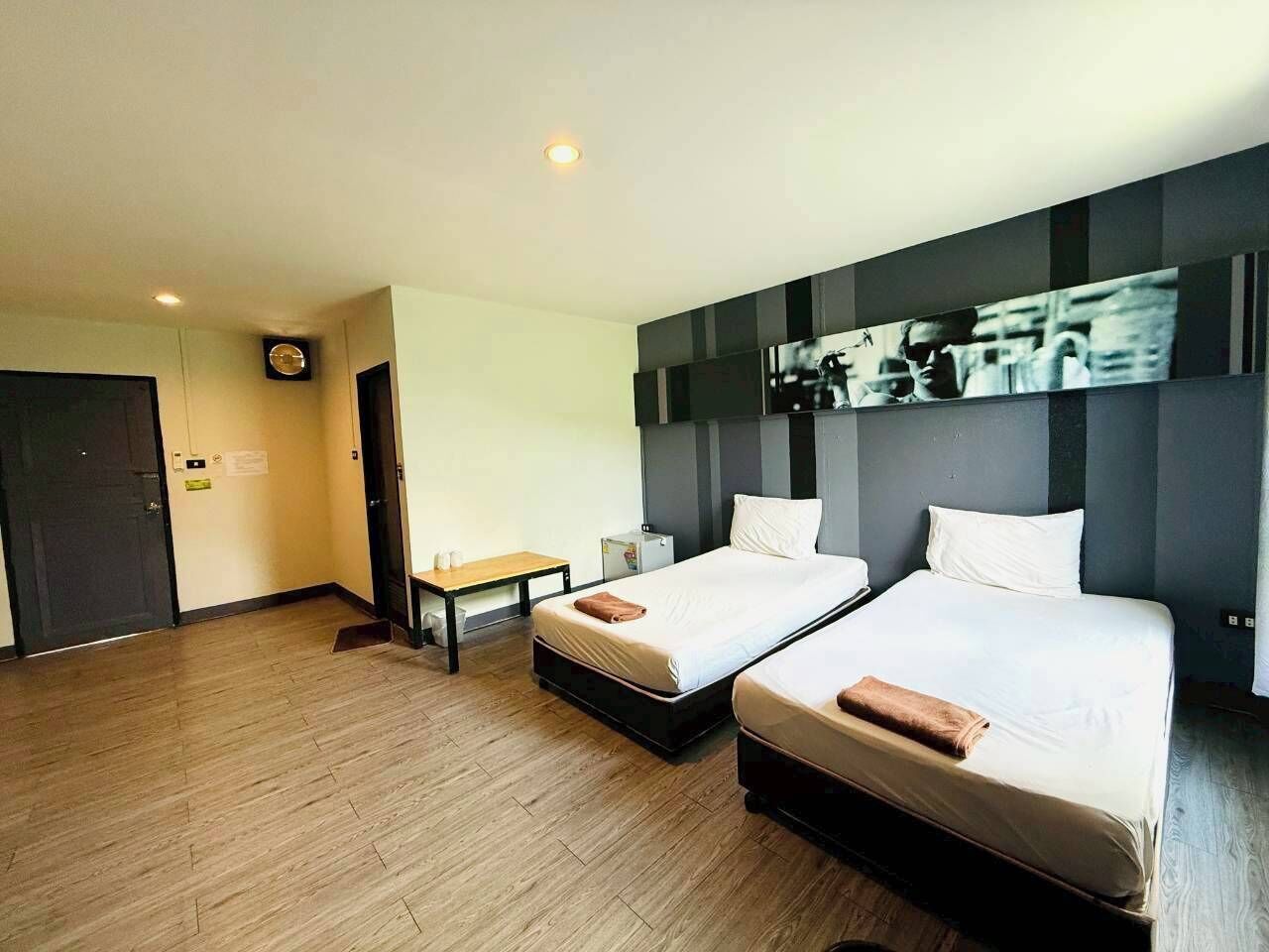 A hotel room with two beds, a desk, a chair, a clock, and a wall-mounted artwork.