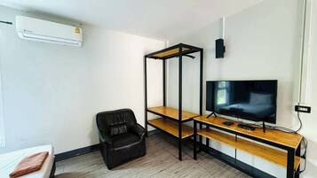 Una habitación con una cama, un sillón de cuero negro, un televisor sobre un soporte de madera y un estante metálico negro.