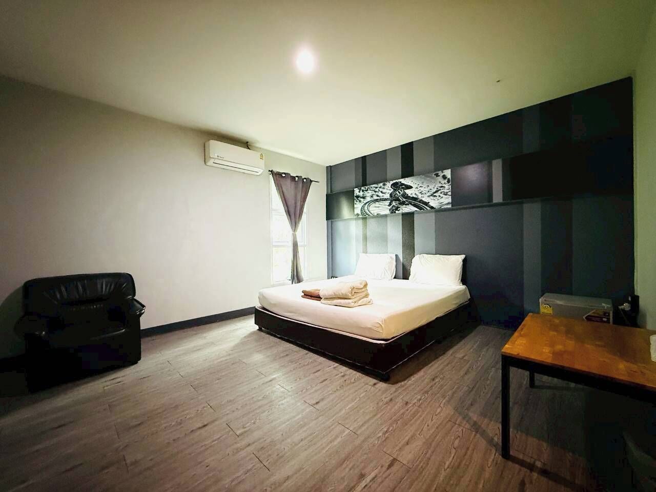 A bedroom with a bed, a wooden floor, a black sofa, a table, and a wall-mounted air conditioner.