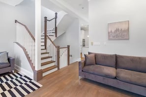 Ein modernes Wohnzimmer mit Treppe, einem grauen Sofa und einem Schachbrettteppich.