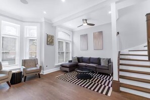 Ein Wohnzimmer mit einem Ecksofa, einem Sessel, einem Couchtisch und einem Streifenmuster-Teppich.