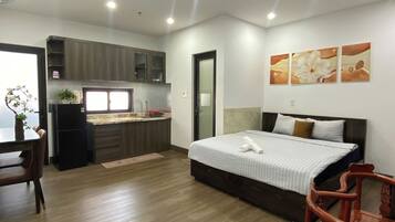 A compact hotel room with a bed, a small kitchenette, a dining area, and a bathroom.