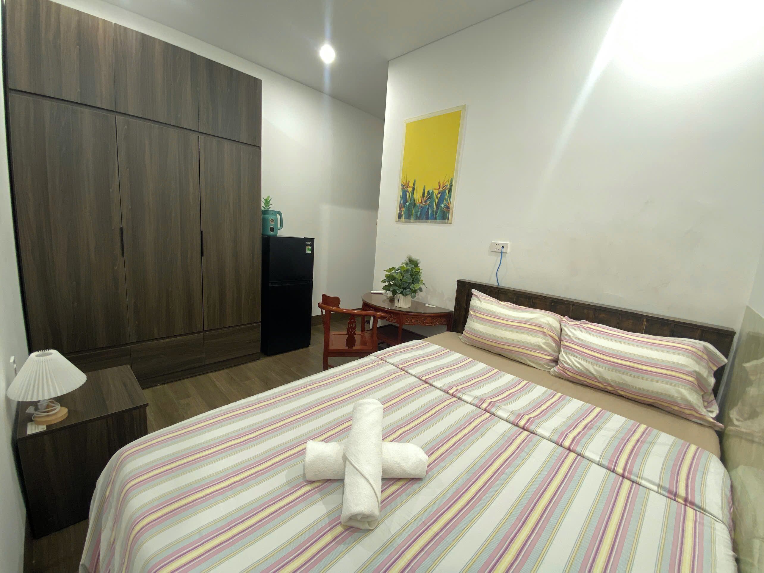 Ein Hotelzimmer mit einem großen Bett, einem Holzschrank, einem kleinen Tisch mit Pflanze und einem Bild an der Wand.