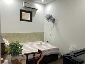 A hotel room with a bed, a desk, a chair, a potted plant, an air conditioner, a wall-mounted fan, and a lamp. - An Thinh Boutique Apartment Da Nang (Da Nang)