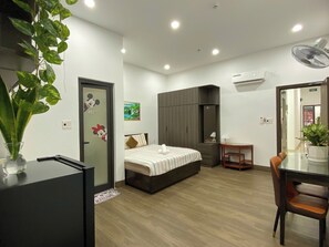 A hotel room with a bed, a desk, a chair, a plant, and a wardrobe. - An Thinh Boutique Apartment Da Nang (Da Nang)
