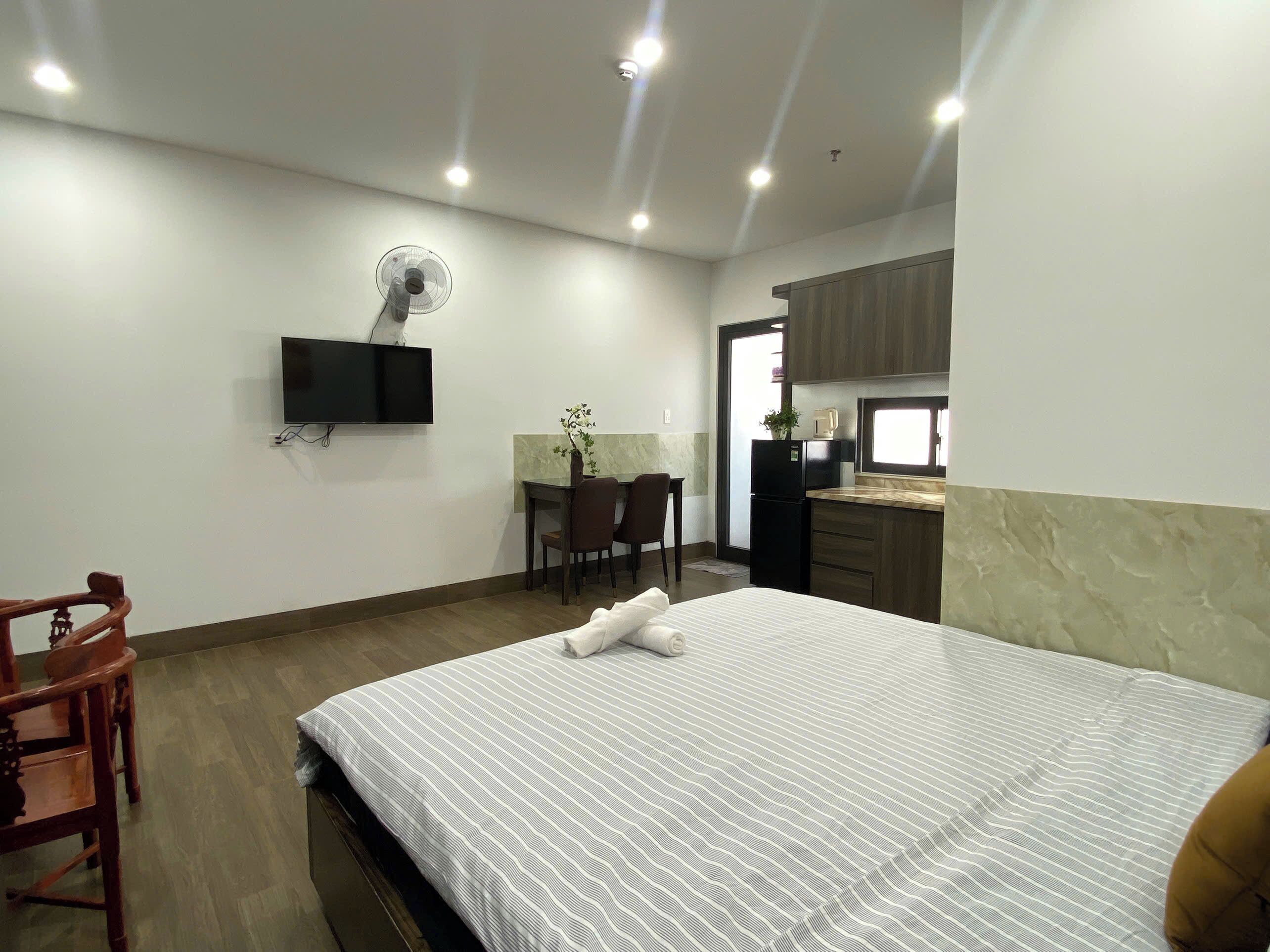 Habitación de hotel con cama, escritorio con silla, televisor montado en la pared y una pequeña cocina.